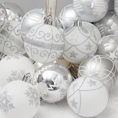 silver and white christmas ornaments are arranged in a pile on the snowflaked ground