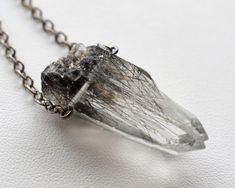 Actinolite Quartz Necklace: This unique crystal necklace is sure to become your new favorite! Inside each crystal lies a stunning lattice of overlapping black actinolite threads. Our classic unisex design makes it the perfect gift for crystal lovers of any gender. ✧ Brazilian actinolite included quartz point ✧ 100% natural raw crystal; not cut or polished ✧ Crystal sizes range from 25-45mm (1-1.75 inches) ✧ Select your favorite crystal from the dropdown menu ✧ Lustrous gunmetal chain in your cho Unique Quartz Crystal Necklace With Gemstone, Spiritual Silver Crystal Necklace With Raw Stone, Mystical Raw Stone Crystal Necklace Gift, Raw Crystal Necklace Pendants, Raw Quartz Stone Pendant Necklace, Character Jewelry, Rutilated Quartz Jewelry, Hardware Jewelry, Mineral Jewelry