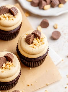 three chocolate cupcakes with peanut butter frosting and chopped peanuts on the side