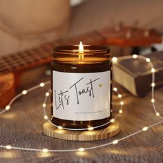 a lit candle sitting on top of a wooden table next to a guitar and string lights