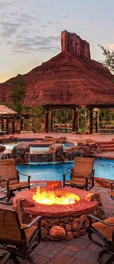 an outdoor fire pit surrounded by chairs and umbrellas with mountains in the back ground