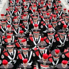 a large group of people dressed in black and red marching uniforms with white trims