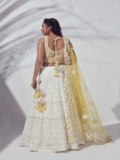 A three-piece Ivory lehenga set from the Suruchi Parakh collection. This elegant ivory georgette lehenga is paired with a hand-embroidered tussar silk blouse. The outfit is completed with a matching yellow net dupatta. The hand-embroidered blouse has a back hook with a tassel opening. And, the dupatta has a beautiful touch of embroidery cutwork. White Organza Lehenga With Chikankari Embroidery, White Organza Cutdana Choli, Designer White Lehenga With Chikankari Embroidery, Designer Chikankari Embroidered White Lehenga, Traditional Cream Georgette Lehenga, Cream Choli With Zari Work In Georgette, Embroidered Off White Georgette Lehenga, Cream Georgette Choli With Zari Work, White Lehenga With Intricate Embroidery In Georgette