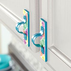 two blue handles are attached to the door handle on a white cabinet with flowers painted on it