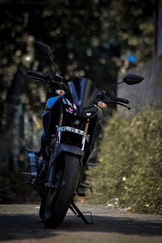 the motorcycle is parked on the side of the road in front of some bushes and trees