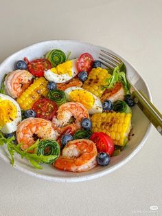 a white bowl filled with shrimp, corn and blueberries on top of a table