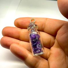 a hand holding a glass bottle filled with purple rocks