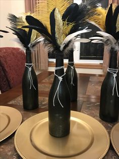 three black vases with gold and white feathers in them are sitting on a table