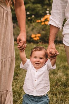 a little boy holding the hands of his parents