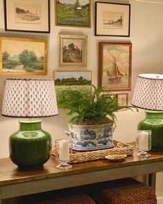 two green vases sitting on top of a wooden table next to lamps and pictures