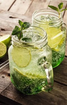 two mason jars filled with lemonade, lime and mint on top of a wooden table