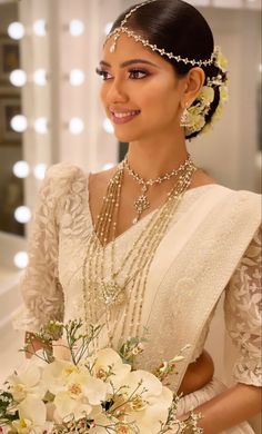 a woman in a white dress holding a bouquet of flowers and pearls on her head