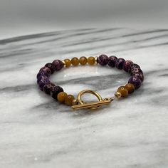 Introducing our meticulously handcrafted bracelet, a luxurious blend of deep, mesmerizing Purple Jasper and the captivating sheen of Gold Tiger Eye beads. This exquisite piece features 8mm Purple Jasper beads known for their grounding and protective properties, paired beautifully with 6mm Gold Tiger Eye beads that are believed to bring courage and confidence to the wearer. Each bead is delicately separated by elegant gold spacers, adding a touch of sophistication and timeless charm. The bracelet is securely fastened with a high-quality gold clasp, ensuring durability and ease of wear. Gold Amethyst Jewelry With 8mm Beads, Spiritual Amethyst Gold Bracelets, Gold Amethyst Beaded Bracelets, Gold Amethyst Bracelets For Healing, Gold Bracelets With Round Amethyst Beads, Gold Amethyst Beaded Bracelets For Jewelry Making, Gold Agate Bracelet With Gemstone Beads, Gold Agate Beaded Bracelets With Gemstones, Gold Agate Gemstone Beaded Bracelets