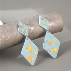 two blue and gold earrings sitting on top of a piece of wood