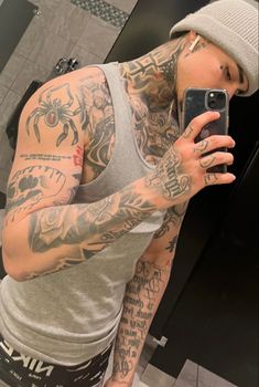 a man with tattoos taking a selfie in the mirror while wearing a hat and holding a cell phone