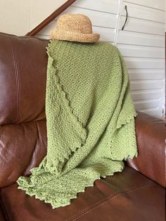 a brown leather chair with a green blanket on it and a hat sitting on top of the couch