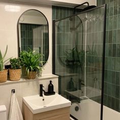 a bathroom with a sink, mirror and bathtub next to a plant filled wall