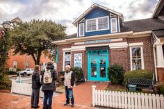 three people standing in front of a building with a blue door and white picket fence