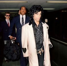 two men in suits are walking through an airport terminal with one man wearing a white coat and black shirt