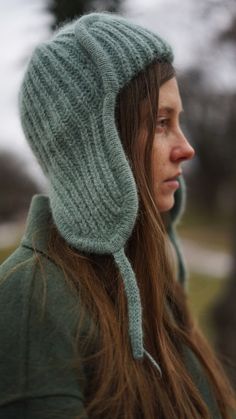 a woman wearing a green hat with a hood on her head and long hair in the wind