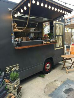 an outdoor food truck with lights hanging from it's roof and tables around it