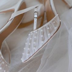 a pair of white shoes with pearls on the heel and straps are sitting on a bed