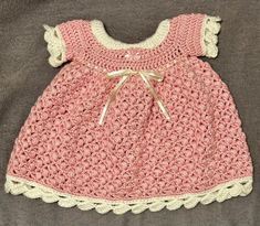 a pink crocheted dress with white trim on the chest and bottom, sitting on a gray surface