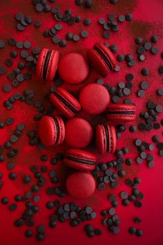 red and black macaroons with chocolate chips scattered around them on a red surface