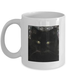 a white coffee mug with a black cat's face and glowing eyes on it