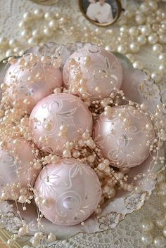 a glass bowl filled with pink ornaments on top of a lace doily covered table