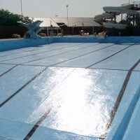 an empty swimming pool with water slides in the backgroud and blue tarps