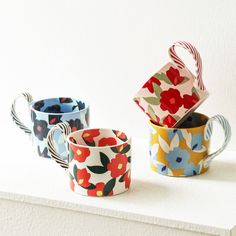 three colorful cups sitting on top of a white counter next to each other and one cup has a flower pattern