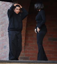 a man and woman standing next to each other in front of a brick wall with their hands on their head