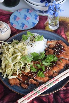 a plate with rice, meat and vegetables next to chopsticks on a table