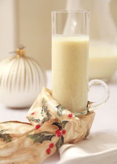 a glass of milk sitting on top of a table next to a napkin and vase