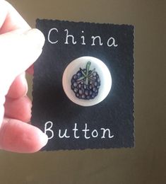 a person holding a button with a small black berry on it and the word china written in white