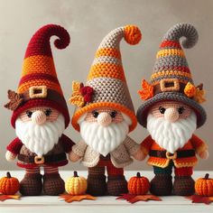 three crocheted gnomes standing next to each other with pumpkins on the ground