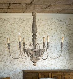 a chandelier hanging from the ceiling in a room with floral wallpaper and wooden furniture