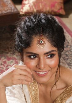 a woman wearing a gold and white sari sitting on top of a carpeted floor