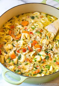 a pot filled with pasta and vegetables on top of a table next to a wooden spoon