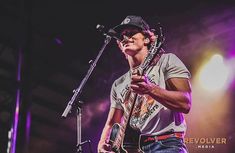 a man standing in front of a microphone holding a guitar and singing into a microphone