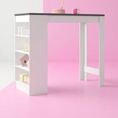 a white desk with shelves and a pink wall in the backround, next to it is a coffee cup