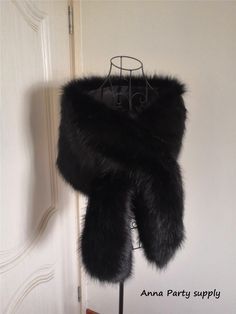 a black fur stole hanging on a metal rack in front of a white wall and door