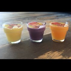 three glasses filled with different colored drinks on top of a wooden table next to each other