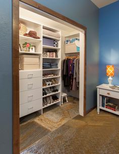 an open closet with clothes and shoes on the shelves next to a dresser, lamp and mirror