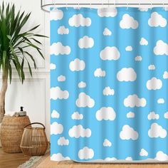 a blue shower curtain with white clouds on it in a room next to a potted plant