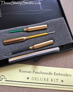 three pens are sitting in a box next to a piece of paper that says russian punch needle embroidery deluxe kit