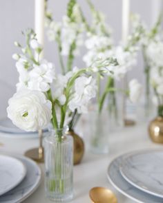 white flowers are in vases on a table with silver and gold place settings for dinner