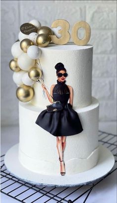 a birthday cake decorated with a woman in black dress and gold balloons on the top