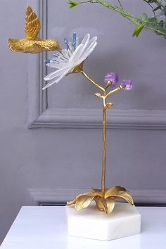 a gold and white flower is sitting on a table next to a potted plant